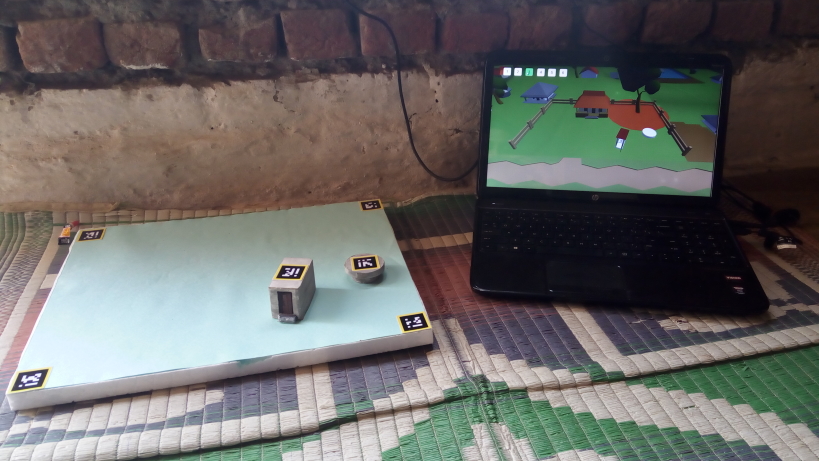 There are two tangible objects, one representing a toilet and the other the soak pit. AR tags placed on top enable tracking of the objects using an overhead camera. Both control the poses of their virtual avatars on the laptop